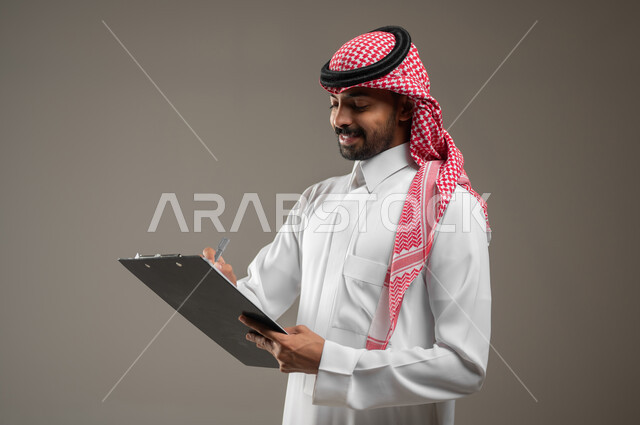 رجل عربي سعودي خليجي باللزي السعودي، مسؤول عن الاشراف على العمل و مراقبة اداء الموظفين ، يسجل ملاحظاته و المهام المطلوبة على ملف خاص، تدوين الملاحظات والسجلات، الرقابه والتحقيق، بورتريه جانبي مقرب، خلفيه رماديه، محتوى حساس