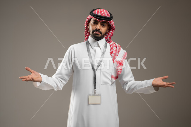 Questioning, questioning, and inquiring about something, gestures of not knowing, astonishment, and astonishment, a close-up portrait of a Saudi Gulf Arab man wearing a shemagh and traditional dress, wearing an identification card, raising his hands up, gestures of explanation and clarification, gray background, sensitive content.