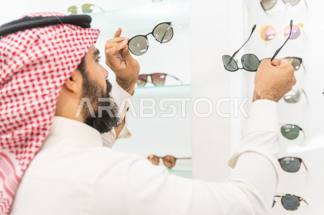 شاب سعودي يقوم باختيار النظارة الشمسية المناسبة في محل نظارات , نظارات شمسية أنيقة . 