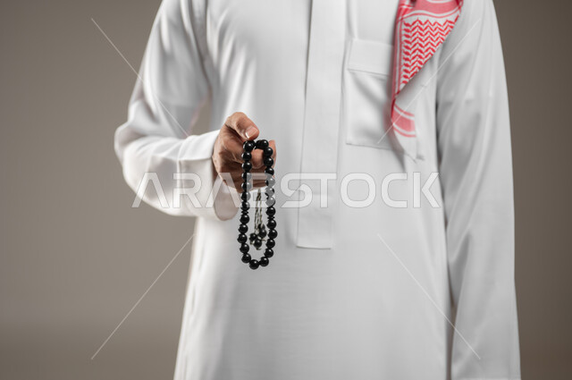 بورتريه مقرب ليد تمسك السبحه لرجل عربي خليجي سعودي، التسبيح وذكر الله تعالى ، أدعية وأذكار، الاستغفار والصلاه عللى النبي محمد صلى الله عليه وسلم، إسلاميات وعبادة ، سبحه باللون الاسود، خلفية باللون الرمادي، محتوى حساس، استخدام حساس
