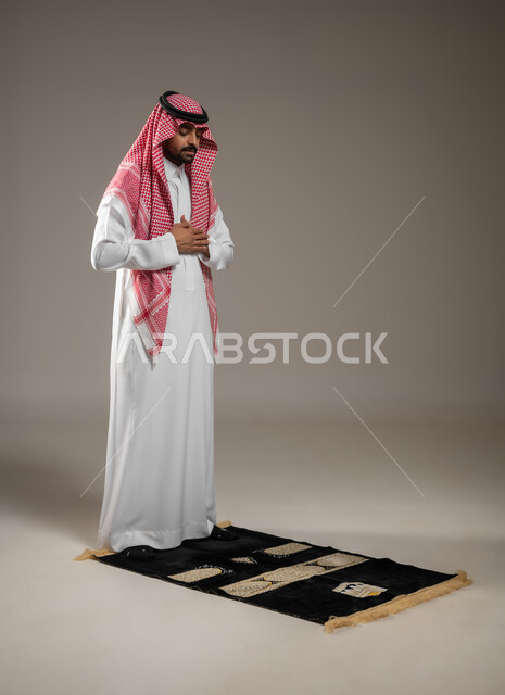 أداء فريضة الصلاه، الركن الثاني من اركان الاسلام، رجل خليجي عربي سعودي يرتدي الثوب والشماغ والعقال السعودي، يصلي على سجاده الصلاه في المصلى، الخشوع في الصلاه، العبادة و التقرب الى الله، بورتريه بالطول جانبي بالطول الكامل، خلفيه رماديه، محتوى حساس