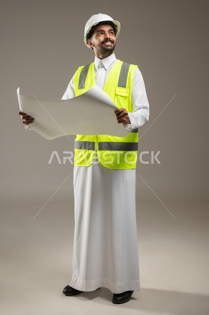 الحرص على بناء الأساسيات الجيده للمبنى، مهندس عربي خليجي سعودي يرتدي الخوذة وسترة الحماية يعمل في القطاع الهندسي، يقوم بدراسه مخططات المشروع، ينظر الى الاعلى للتاكد من جوده الاساسات الهندسيه، بورتريه جانبي بالطول الكامل، خلفيه رماديه، محتوى حساس