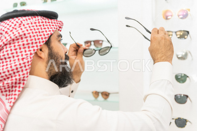 شاب سعودي يقوم باختيار النظارة الشمسية المناسبة في محل نظارات , نظارات شمسية أنيقة . 