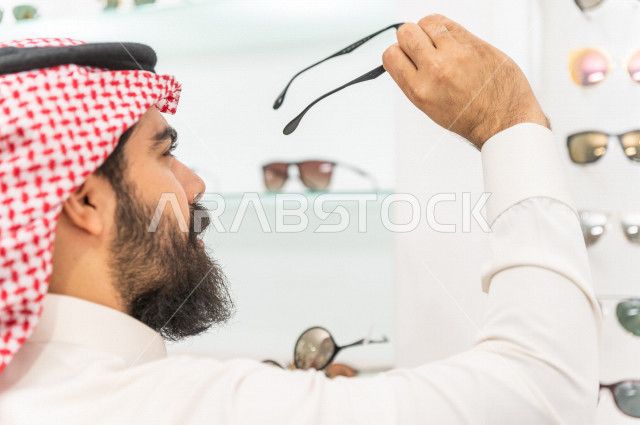 A young Saudi man selects the appropriate sunglasses in an eyewear store, stylish sunglasses.