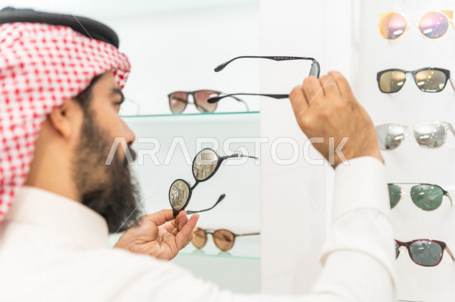 شاب سعودي يقوم باختيار النظارة الشمسية المناسبة في محل نظارات , نظارات شمسية أنيقة . 