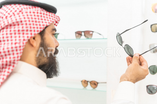 شاب سعودي يقوم باختيار النظارة الشمسية المناسبة في محل نظارات , نظارات شمسية أنيقة . 