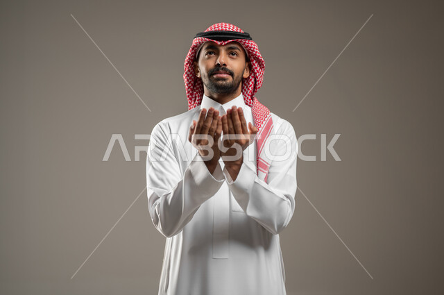 اشارات وجه ويدين تدل على الدعاء، التضرع الى الله, بورتريه لرجل عربي خليجي سعودي ينظر الى الاعلى، الحمد والشكر و طلب العون, الرغبه في تحقيق الأمنيات, يرفع يديه للاعلى، يطلب العون والمغفره من الله، خلفيه رماديه، محتوى حساس، استخدام حساس