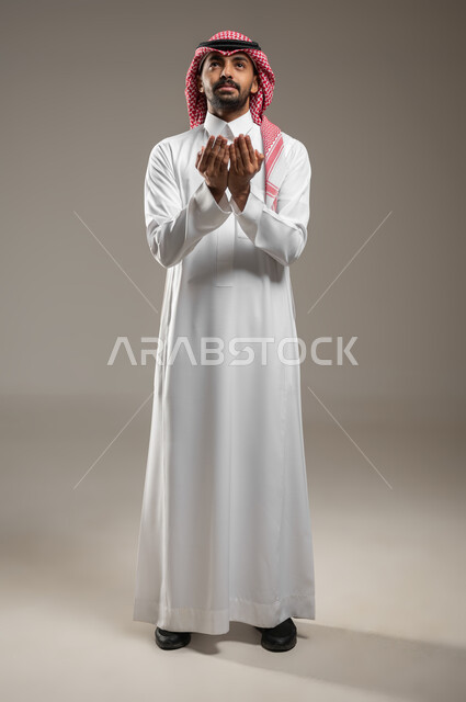 اشارات وجه ويدين تدل على الدعاء، التضرع الى الله, بورتريه لرجل عربي خليجي سعودي ينظر الى الاعلى، الحمد والشكر و طلب العون, الرغبه في تحقيق الأمنيات, يرفع يديه للاعلى، يطلب العون والمغفره من الله، صوره الجسم بالطول الكامل، خلفيه رماديه، محتوى حساس
