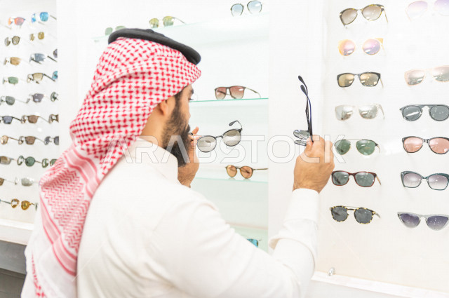 A young Saudi man selects the appropriate sunglasses in an eyewear store, stylish sunglasses.