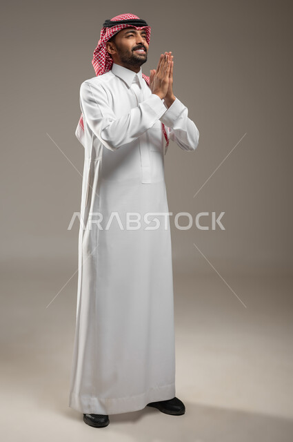طلب العطف والمساعدة، بورتريه لرجل عربي خليجي سعودي يرتدي الشماغ والثوب السعودي،  يرفع يده لاعلى بإيماءات الدعاء والتوسل، حركة يد تدل على الاسترحام والترجي، صوره الجسم بالطول الكامل، استخدام حساس، محتوى حساس