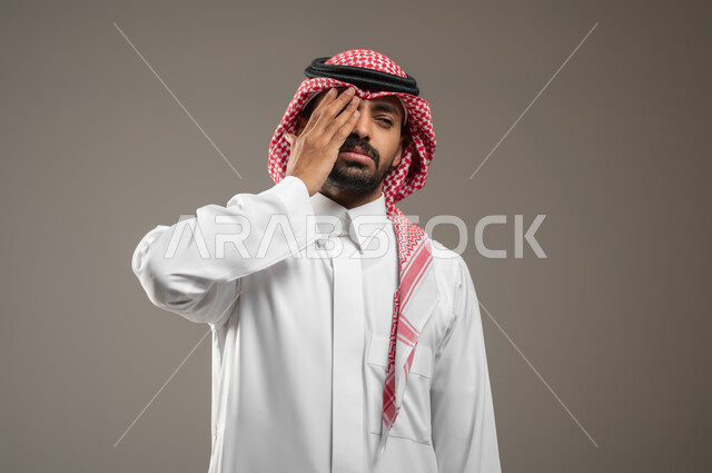 الشعور بألم في العين , إجراء فحص طبي, بورتريه مقرب لرجل عربي خليجي سعودي يرتدي الزي السعودي، يغطي عينه بيده، ايماءات وجه ويد تدل على اجراء الفحص الطبي للعين، التعتيم وضعف الرؤيا، الشعور بالالم والصداع، خلفيه رماديه، استخدام حساس، محتوى حساس