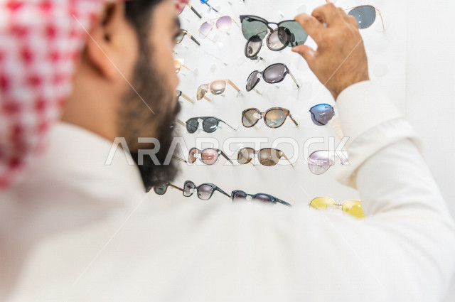شاب سعودي يقوم باختيار النظارة الشمسية المناسبة في محل نظارات , نظارات شمسية أنيقة . 