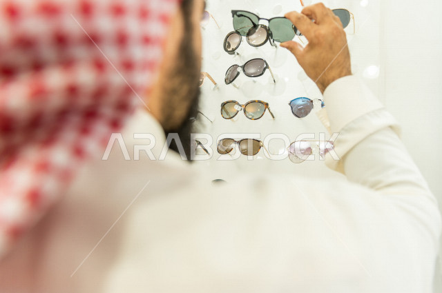 شاب سعودي يقوم باختيار النظارة الشمسية المناسبة في محل نظارات , نظارات شمسية أنيقة . 