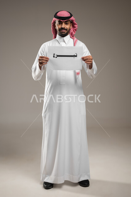 الأعمال الخيرية الإسلاميه، المساعدات والتبرعات الإنسانية، بورتريه  لرجل عربي سعودي خليجي يرتدي الثوب والشماغ السعودي و يمسك بيده ورقه مكتوب بها تبرع، الدال على الخير كفاعله، صوره الجسم بالطول الكامل، خلفية رمادية، استخدام حساس، محتوى حساس