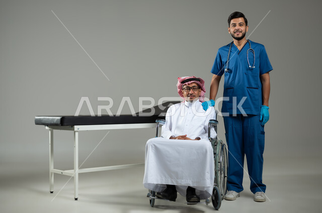 الاهتمام بصحة المرضى، النظر إلى الكاميرا بإيماءات السرور، بورتريه لممرض يرتدي اليونيفورم يضع يديه على كتف رجل عربي خليجي سعودي يرتدي الزي التقليدي والشماغ يجلس على الكرسي المتحرك ، صورة الجسم بالطول الكامل، خلفية رمادية، محتوى حساس ، استخدام حساس