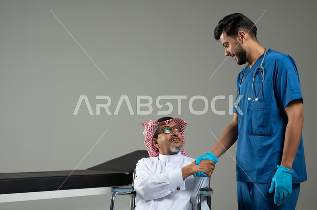 تقديم أفضل الخدمات الصحية لمرضى كبار السن في المستشفى، بورتريه لرجل عربي خليجي سعودي يرتدي الزي التقليدي والشماغ يجلس على الكرسي المتحرك يصافح الممرض ، شكر وتقدير الطبيب لجهوده ورعايته الطبية ، خلفية رمادية، محتوى حساس ، استخدام حساس