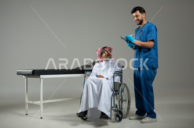 الوقوف باستقامة وتقديم الخدمات الصحية والطبية، بورتريه لطبيب عربي خليجي سعودي يرتدي اليونيفورم يقوم بتدوين المعلومات العامة لمريض مسن يرتدي الثوب التقليدي والشماغ يجلس على سرير المرضى, الجسم بالطول الكامل، خلفية رمادية، محتوى حساس ، استخدام حساس