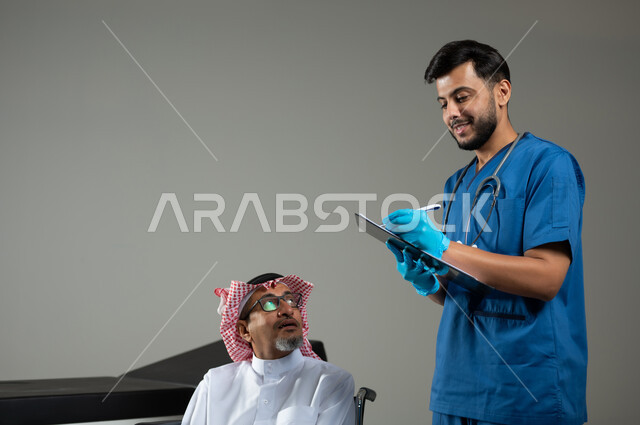تقديم الخدمات الطبية، بورتريه مقرب لممرض عربي خليجي سعودي يرتدي اليونيفورم يقوم بتدوين المعلومات العامة لمريض مسن يرتدي الثوب التقليدي والشماغ يجلس كرسي متحرك، خلفية رمادية، محتوى حساس ، استخدام حساس