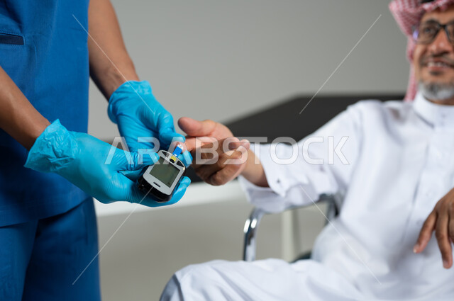 استخدام جهاز السكري الالكتروني، بورتريه مقرب لممرض يرتدي اليونيفورم يقوم بفحص نسبة السكر لرجل عربي خليجي سعودي يرتدي الثوب التقليدي والشماغ يجلس على الكرسي المتحرك، العمل في القطاع الصحي، خلفية رمادية، محتوى حساس، استخدام حساس