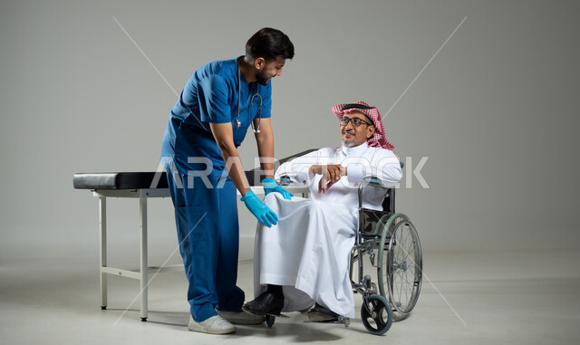 تقديم الخدمه والاحتياجات الخاصة بكل كفاءة، مفهوم الطب والرعاية الصحية، بورتريه لممرض عربي خليجي يرتدي اليونيفورم يقوم بفحص مفاصل مريض سعودي مقعد يرتدي الثوب التقليدي يجلس على الكرسي المتحرك، الجسم بالطول الكامل، خلفية رمادية ، محتوى حساس، استخدام حساس .