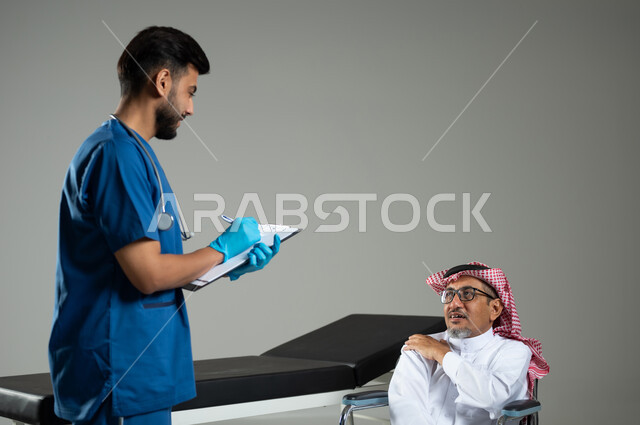 دراسة و مراجعة حالات المرضى، العمل في القطاع الصحي في السعودية،  بورتريه مقرب لطبيب عربي خليجي سعودي يرتدي اليونيفورم يقوم بتدوين المعلومات العامة لمريض مسن يرتدي الثوب التقليدي والشماغ يجلس على كرسي متحرك، خلفية رمادية، محتوى حساس ، استخدام حساس