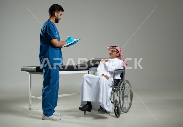 العمل في القطاع الصحي في السعودية،  بورتريه لطبيب عربي خليجي سعودي يرتدي اليونيفورم يقوم بتدوين المعلومات العامة لمريض مسن يرتدي الثوب التقليدي والشماغ يجلس على كرسي متحرك, الجسم بالطول الكامل، خلفية رمادية، محتوى حساس ، استخدام حساس