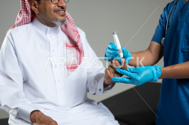 العمل في القطاع الصحي في السعودية، استخدام جهاز الفحص الالكتروني السكري، بورتريه مقرب لممرض عربي خليجي سعودي يرتدي اليونيفورم الطبي يقوم بفحص نسبة سكر الدم لمريض كبير بالسن مبتسم يجلس على سرير المرضى, خلفية رمادية, محتوى حساس، استخدام حساس