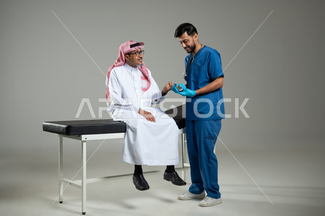 Medical services and examinations, working in the health sector in Saudi Arabia, a portrait of a nurse wearing protective gloves checking the blood sugar level of a sick Saudi Arab Gulf man wearing traditional clothing sitting on a patients’ bed, full length of the body, gray background, sensitive content, sensitive use