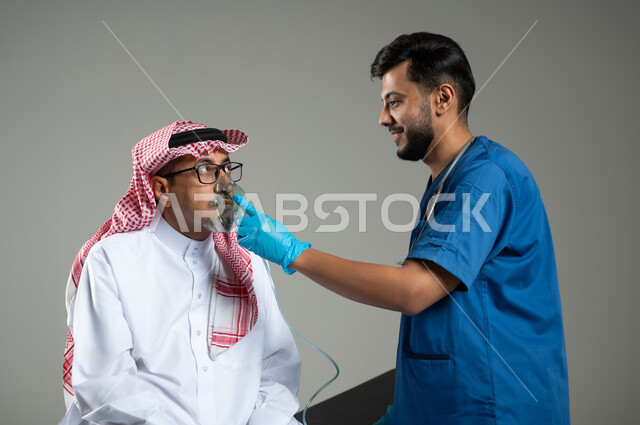 معالجة أمراض الربو المزمنة، المحافظة على ممر هوائي منتظم باستخدام جهاز التنفس الصناعي، بورتريه مقرب لممرض عربي خليجي سعودي يرتدي اليونيفورم يقوم باعطاء ادوية الكحة لرجل مسن ، تقديم الخدمات الصحية للمريض، خلفية رمادية، محتوى حساس، استخدام حساس