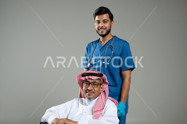 الاهتمام والاعتناء بمرضى ذوي الهمم، تقديم الخدمات والاحتياجات الخاصة بكل كفاءة،  بورتريه مقرب لطبيب عربي سعودي خليجي يشرف على علاج رجل مسن مريض يجلس على كرسي متحرك ،النظر إلى الكاميرا بإيماءات السرور، خلفية رمادية، محتوى حساس، استخدام حساس