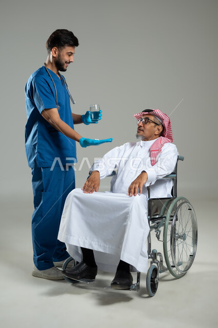 The concept of medicine and health care, using prescription medication and taking care of a patient in a wheelchair, portrait of a smiling Saudi Arabian Gulf doctor wearing a uniform giving medications to an elderly patient wearing a traditional dress, full-length body, gray background, sensitive content, sensitive use.