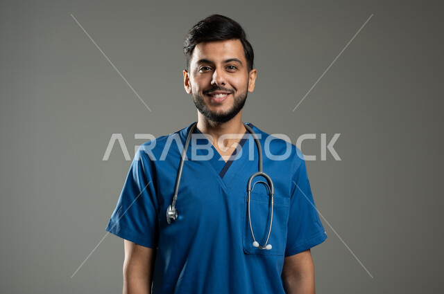 الاستعداد لتقديم الخدمات للمرضى بكل كفاءه ،مفهوم الطب والرعاية الصحية، النظر إلى الكاميرا بإيماءات السرور، بورتريه مقرب لممرض عربي خليجي سعودي مبتسم يرتدي اليونيفورم يضع سماعة الفحص، خلفية رمادية، خلفية رمادية، محتوى حساس، استخدام حساس