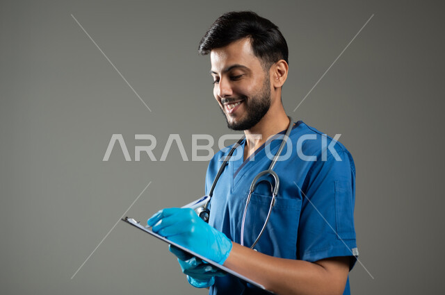 العمل في القطاع الصحي في السعودية، تقديم الخدمات الطبية، تدوين المعلومات العامة عن حالة المريض، بورتريه مقرب لممرض عربي خليجي سعودي مبتسم يرتدي اليونيفورم يضع سماعة الفحص، خلفية رمادية، محتوى حساس، استخدام حساس
