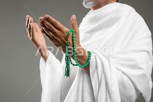 القيام بالتسبيح وقراءة أذكار ما بعد الصلاة, أداء مناسك الحج والعمرة، بورتريه مقرب لرجل مسلم عربي سعودي خليجي يرتدي ملابس الاحرام ويحمل بيده سبحة خضراء، خلفية رمادية، محتوى حساس، استخدام حساس