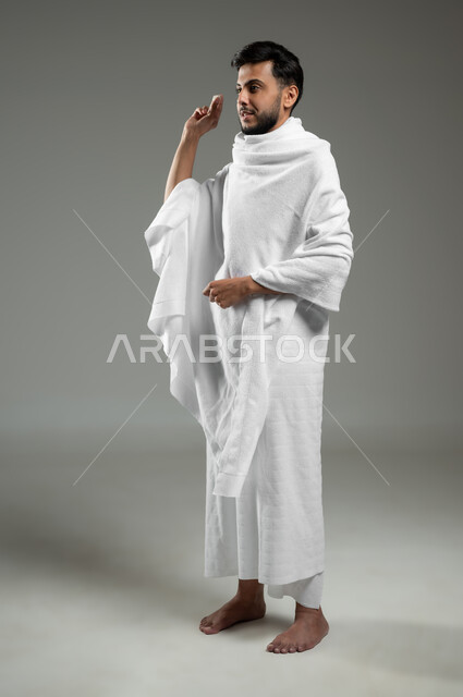 Performing Hajj and Umrah rituals, throwing Jamarat al-Aqaba on the Day of Sacrifice, portrait of a Saudi Arab Gulf Muslim man wearing Ihram clothing holding a pebble in his hand to stone Satan, worship and getting closer to God, full-length body, gray background, sensitive use, sensitive content