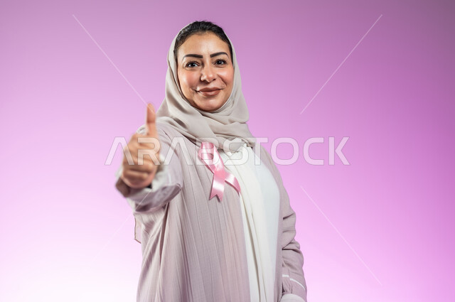 الاعجاب بشعار الحملة العالمية لتحدي الأمراض الخبيثة، بورتريه مقرب لامرأة عربية خليجية سعودية مبتسمة محجبة ترتدي العباءة ترفع اصبع الابهام بتعابير الرضا والجودة، خلفية ورديه، محتوى حساس، استخدام حساس