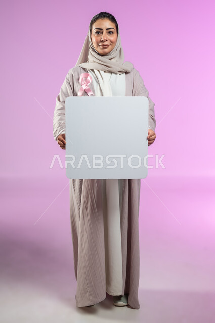 ايماءات السرور والسعادة، موك أب أبيض فارغ مربع الشكل، شعار الحملة العالمية لتحدي الأمراض الخبيثة، لوحة بيضاء إعلانية فارغة للتوعية بسرطان الثدي, بورتريه مقرب لامرأة عربية خليجية سعودية مبتسمة ترتدي العباءة الملونة، خلفية ورديه، محتوى حساس، استخدام حساس