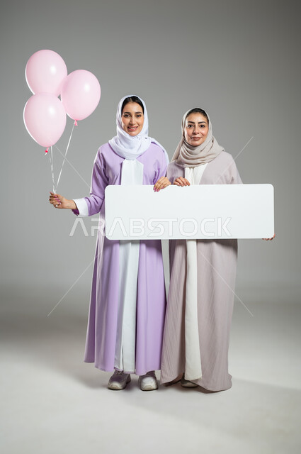 لوحات إعلانية للتوعية ضد الأمراض الخبيثة، شعار الحملة العالمية لتحدي سرطان الثدي، بورتريه لامراتان عربيتان خليجيتان سعوديتان محجبتان ترتديان العباءه الملونه، الامساك بموك أب مستطيل فارغ وبلالين وردية، الجسم بالطول الكامل,خلفية رمادية، محتوى حساس، استخدام حساس