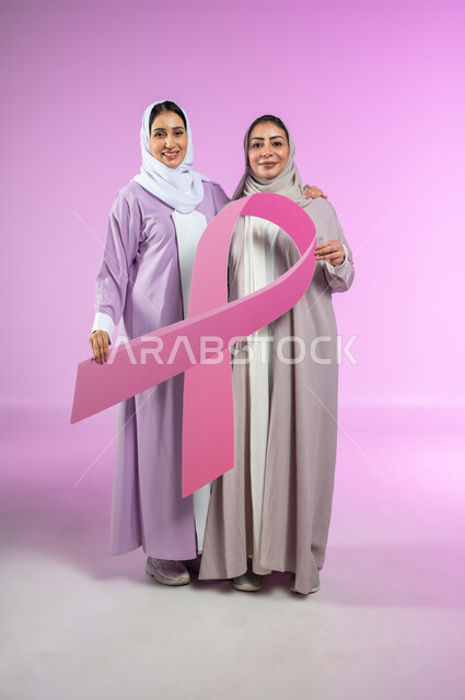 تحدي الأمراض الخبيثة, شعار الحملة العالمية لتحدي سرطان الثدي  بورتريه لامراتان عربيتان خليجيتان سعوديتان محجبتان ترتديان العباءه الملونه تمسكان  بشعار الحملة العالمية، الجسم بالطول الكامل، خلفية ورديه، محتوى حساس، استخدام حساس
