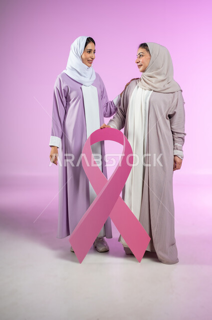 اليوم العالمي للكشف المبكر عن سرطان الثدي,  تحدي الأمراض الخبيثة, بورتريه لامراتان عربيتان خليجيتان سعوديتان محجبتان ترتديان العباءه الملونه تمسكان  بشعار الحملة العالمية، الجسم بالطول الكامل، خلفية ورديه، محتوى حساس، استخدام حساس