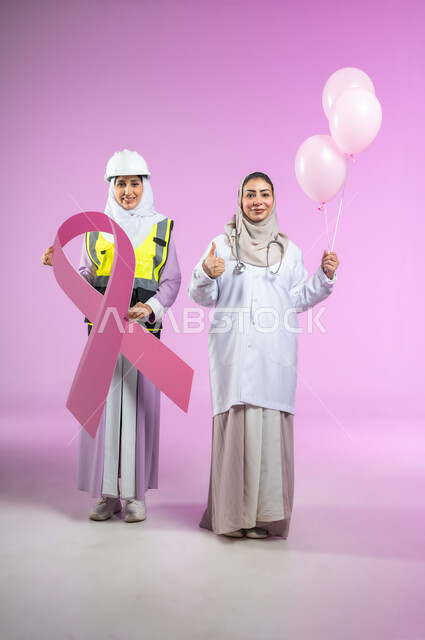 Looking at the camera, World Breast Cancer Day, portrait of a Saudi Gulf Arab doctor wearing a white coat standing with an engineer bearing the slogan of awareness of early detection of malignant diseases, gestures of pleasure and joy, full-length body, pink background, sensitive content, sensitive use
