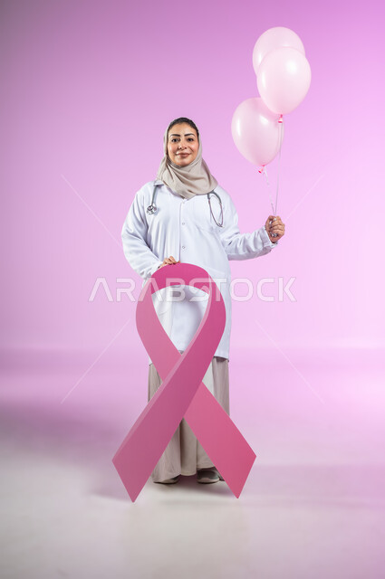 تحدي الأمراض الخبيثة, اليوم العالمي للتوعية والكشف المبكر عن سرطان الثدي, بورتريه لإمرأة عربية خليجية سعودية مبتسمة ترتدي المعطف الأبيض والسماعة الطبية تمسك بيدها البلالين الوردية وشعار الحملة العالمية, الجسم بالطول الكامل, خلفية ورديه, محتوى حساس, استخدام حساس