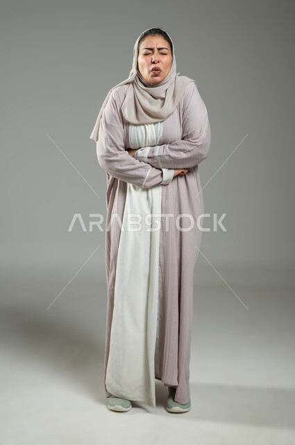 Feeling heartburn and indigestion, the need for help and seeking treatment, the feeling of colic and pain, a portrait of a Saudi Arabian Gulf woman wearing an abaya and veil, placing her hand on her stomach, bending over from the severity of the pain, gestures of vomiting and nausea, a picture of the entire body, gray background, sensitive content, sensitive use