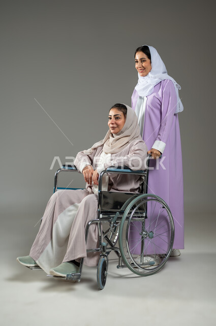 Disabled people’s feeling of belonging and appreciation, taking care of people of determination, a portrait of a veiled Saudi Gulf Arab young woman wearing an abaya, helping a woman with special needs, providing devices and equipment that assist with movement and movement, full-length body, gray background, sensitive content, sensitive use