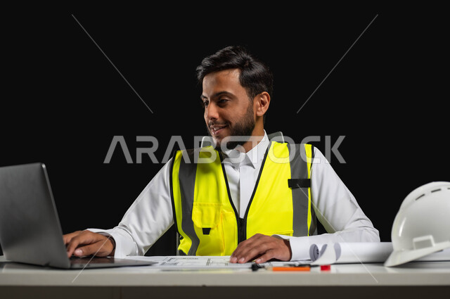 استثمار التكنولوجيا والتقنيات الحديثة في تطور المملكة العربية السعودية,  بورتريه مقرب لمهندس عربي خليجي سعودي  يرتدي الثوب التقليدي و السترة الخاصة بالعمل يجلس على المكتب وأمامه مخططات هندسية معمارية, خلفية سوداء، استخدام حساس، محتوى حساس