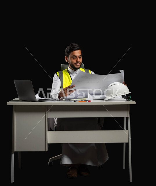 Preview of the implementation of basic plans and projects, growth and development of engineering fields, a portrait of a Saudi Arabian Gulf engineer wearing the traditional dress and work jacket, sitting at the desk and holding engineering plans in his hand, full-length body on a black background, sensitive content, sensitive use