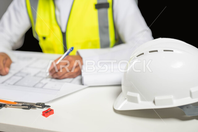 تدقيق ومراجعة المخططات الإنشائية, بورتريه مقرب  لمهندس عربي خليجي سعودي يرتدي الثوب التقليدي و سترة الحماية يسجل على مخطط الإعمار, إدارة المشاريع الهندسية, مهن ووظائف سعودية, العمل في القطاع الهندسي, خلفية سوداء، محتوى حساس، استخدام حساس