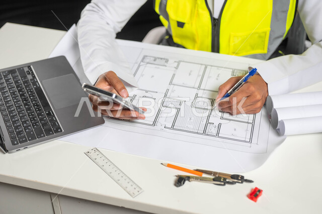 Renaissance in the field of engineering construction, contribution to the development of the engineering sector, close-up portrait of a Saudi Gulf Arab engineer wearing a work jacket, sitting at the desk and holding pens in his hand to complete the drawing of the architectural plan, supervising the project, black background, sensitive content, sensitive use