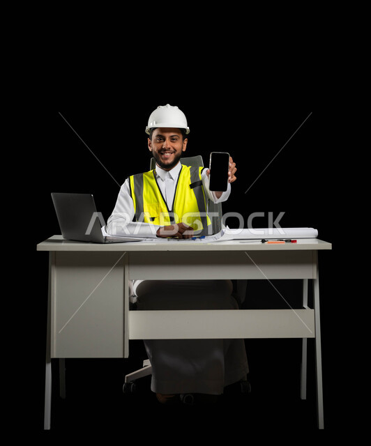 النظر إلى الكاميرا بإيماءات السرور، دمج التقنية والتكنولوجيا في مجال الهندسة، عرض شاشة سوداء فارغة، بورتريه لمهندس عربي خليجي سعودي يرتدي الثوب التقليدي مع الخوذة وسترة الحماية يجلس خلف المكتب، الجسم بالطول الكامل، خلفية سوداء، استخدام حساس، محتوى حساس