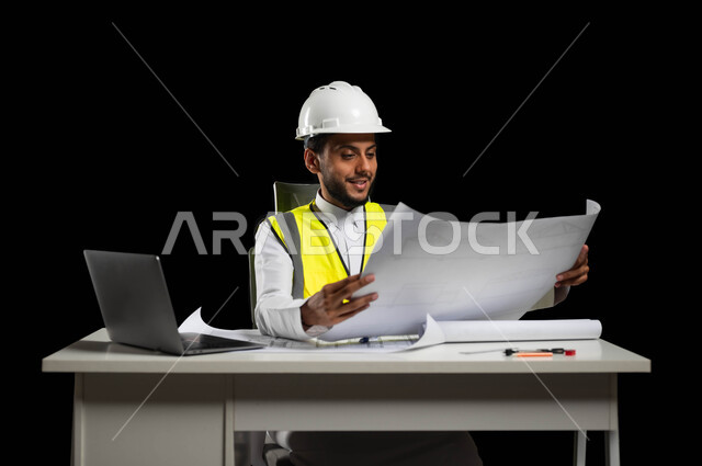 Renaissance in the field of engineering and architectural construction in Saudi Arabia, a portrait of a Saudi Gulf Arab engineer wearing a protection jacket and helmet holding construction plans in his hands, looking at the plan with pride and great happiness, reviewing and displaying project manuscripts completely, project management and follow-up, black background